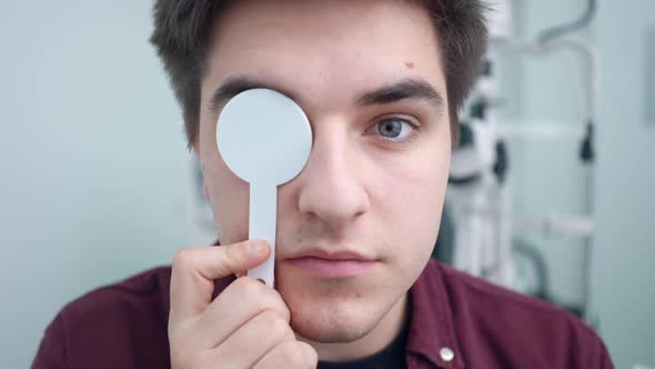 Closeup Headshot of Concentrated Man Closing Eyes One By One with Tool Checking Eyesight in Hospital