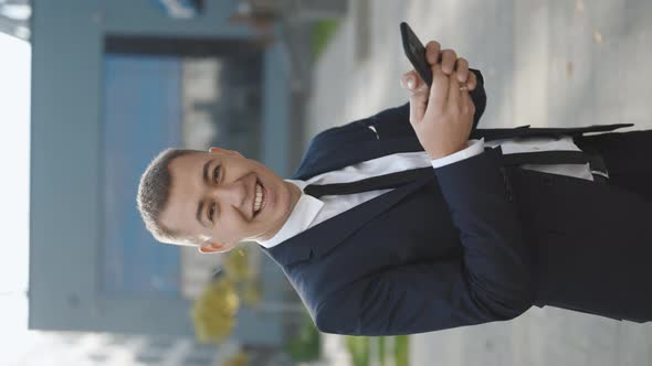 Vertical Video of Handsome Caucasian Businessman is Holding His Smartphone Smiling Charmingly