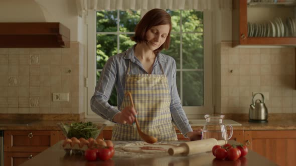 30s Woman Spreading Tomato Sauce for Pizza Standing in the Kitchen