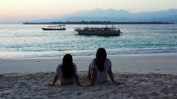 Girls tanning on marine lagoon beach break by blue water with white sandy background of Gili Trawang