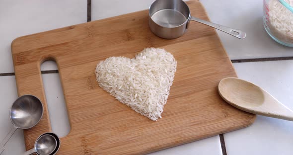 White rice grain in a heart with cooking utensils and ingredients in a kitchen.