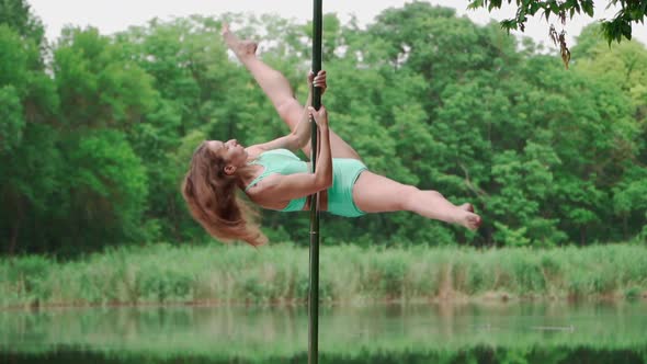 Beautiful Woman with Slim Body Dancing on Background Forest and Lake. Pole Dancer Performs Tricks