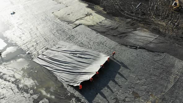 Builders Pull Foil Along Area with Tar at Construction Site