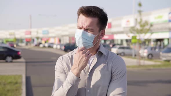 A Young Caucasian Man in a Face Mask Thinks About Something in an Urban Area