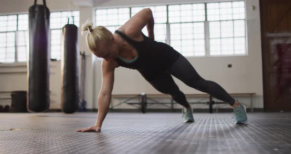 Fit caucasian woman performing one handed push up exercise at the gym