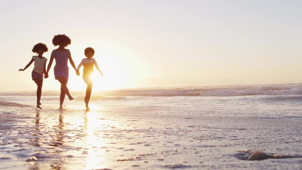 African american mother son and daughter having fun walking together during sunset on the beach