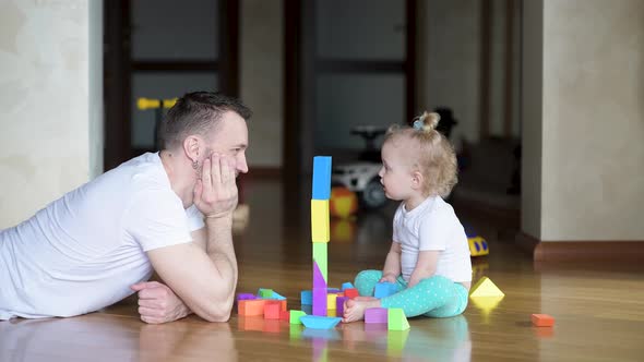 Father is playing with a little daughter on the floor with colored figures