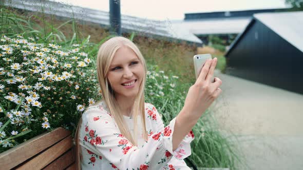 Lovely Young Woman Using Smartphone To Make Video Call While Sitting on Bench on Living Roof of Huge
