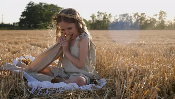 Serious Child Girl with Long Hair Sits on a Mown Wheat Field