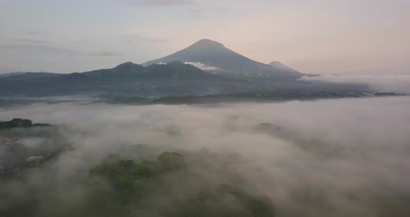 Drone flight over white clouds showing summit of Mount Sumbing in Indonesia during sunset