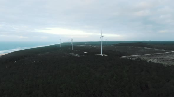 Windmills Rotate on Endless Ocean Shore Under Cloudy Sky