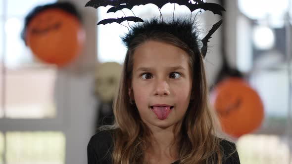 Headshot Cute Caucasian Girl in Bat Headband Halloween Costume Grimacing Looking at Camera Crossing