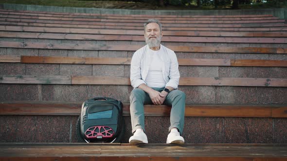 Bearded Pensioner Sits on Stairs Step Near Electric Unicycle