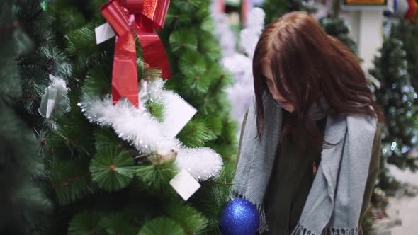 A Young Beautiful Woman Walks Around the Store and Selects Christmas Decorations and Decorations to