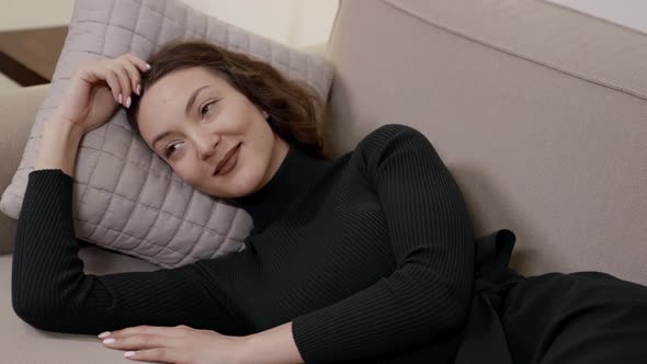 A Happy Woman Lying on a Sofa on a Pillow Enjoying a Rest in a Bright Room