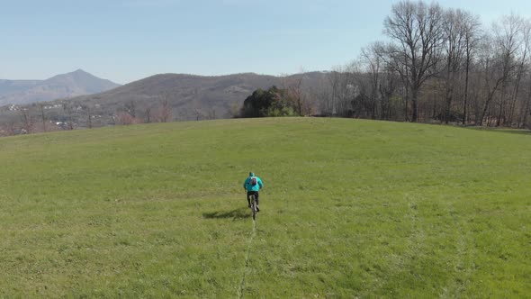 Aerial: man having fun by riding mountain bike in the grass on sunny day, scenic alpine landscape,