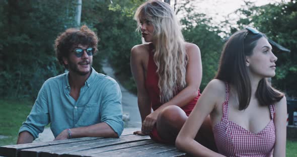 Young friend group talking in nature while sitting at a bench