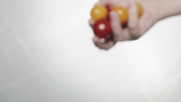 Person Throws Red and Yellow Cherry Tomatoes Into Water