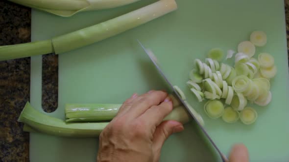 Woman cuts fresh leeks in a green plastic cutting board