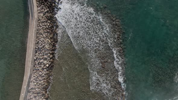 Stone breakwater with Mediterranean sea waves hitting coastline, top down aerial view