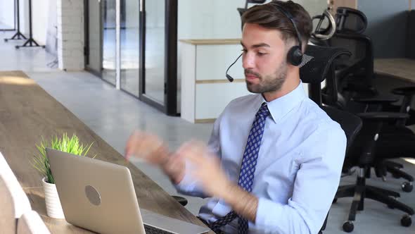 Cheerful young support phone male operator in headset, at workplace while using laptop