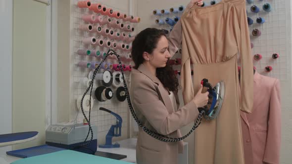 dressmaker steams a new tailored dress by specialized iron steamer in a sewing workshop