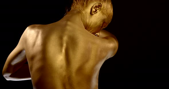 Naked Woman with Golden Skin Is Moving in Black Background Indoors, Back View