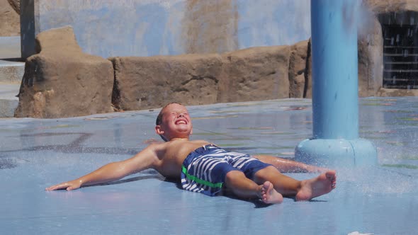 Boy laying down and getting splashed at fountain on summer day, slow motion