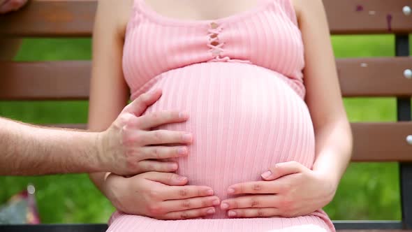 Close Up of Pregnant Woman Hands Stroking Belly on a Park Bench in the Summer