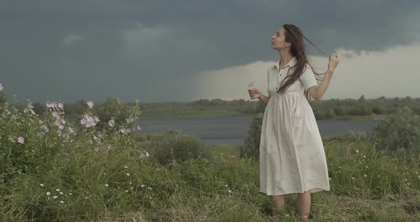 Elegant Girl Stroking Long Hair on Summer Wind Rainy Country Landscape Background. Young Woman in