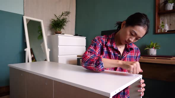 Asian woman assembling furniture alone at home