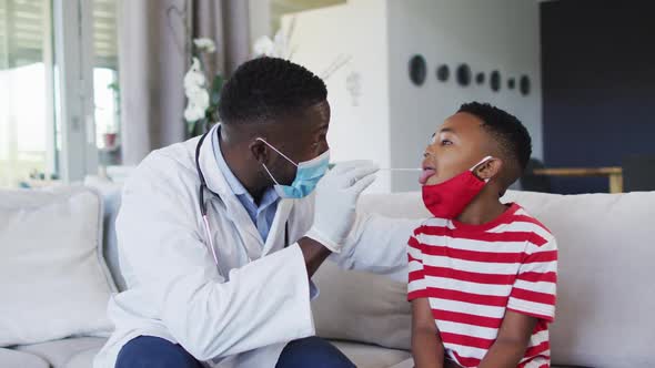 African american doctor wearing face mask taking a throat swab sample of boy at home