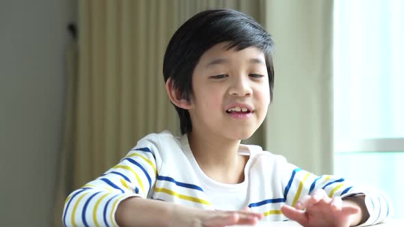 Asian Child Knocking His Hands On The Table.