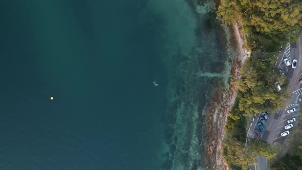 Static high drone view looking down on a coastal headland next to a carpark and road with scuba dive