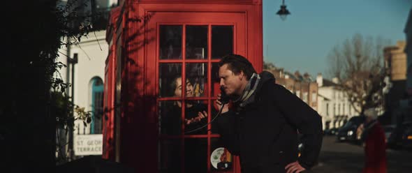 Man talking by phone through the window of a phone booth