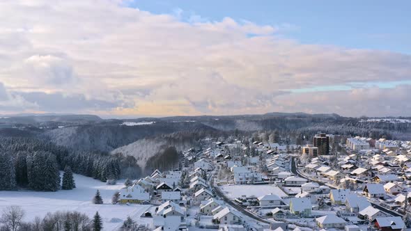Idyllic winter cityscape, snow covered houses inside a valley and sunshine over hillsided trees and