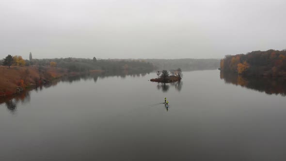 Man and Woman on Sup Paddle Boards at Wide River with Small Island on Golden Autumn Forest