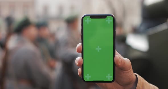 Closeup of a Man's Hand Holding a Mobile Telephone with a Vertical Green Screen on the Streets