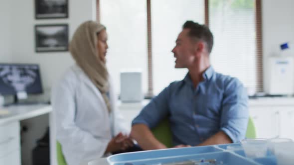 Biracial female dentist talking with male patient at modern dental clinic