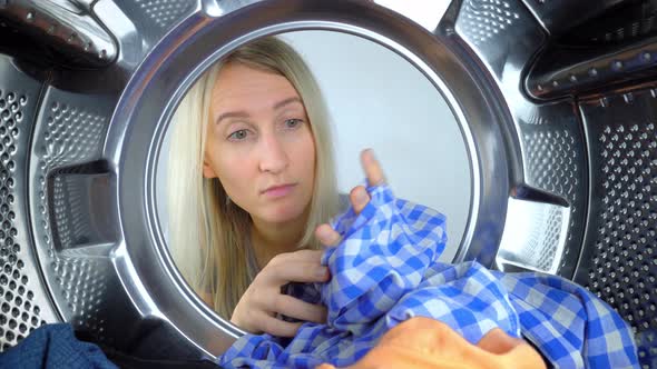 Woman pulls out of washing machine spoiled and torn clothes.