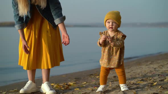 Mom Holds Her Daughter By the Hand and Teaches Her To Walk on Beach