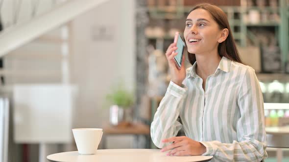 Cheerful Young Latin Woman Talking on Smartphone in Cafe 