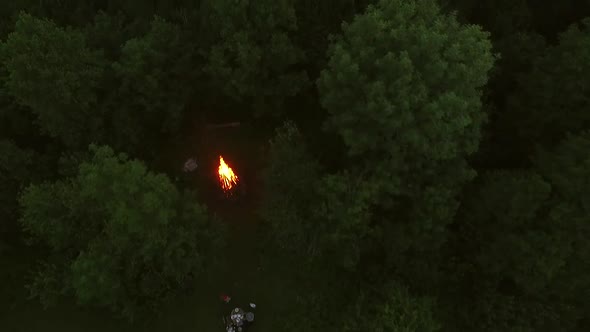 Aerial view of friend eating close to campfire in forest.