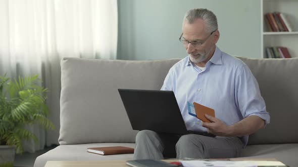 Satisfied Old Man Booking Hotel Room on Laptop, Holding Passport and Tickets