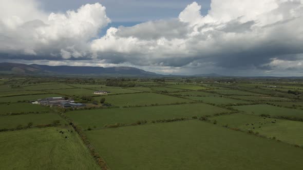 Drone shot of a vast rural Irish landscape with green fields, a farm and hills in the distance.