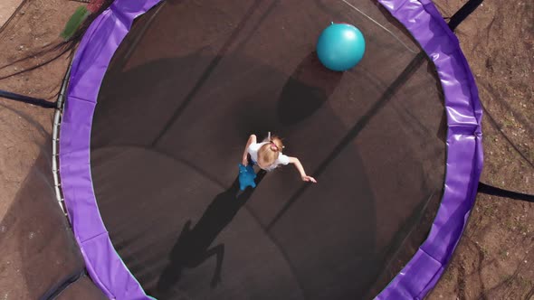 Blonde Child Girl Having Fun Jumping in Trampoline Kicks Balls on Sunset Top Angle