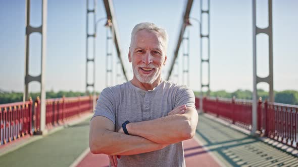 Greyhaired Man Crosses Arms Looking in Camera and Smiling