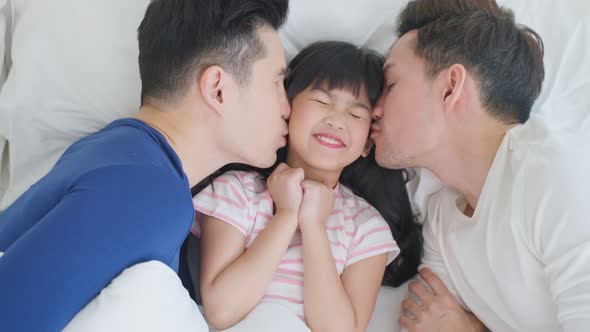 Portrait of handsome man gay family with young kid daughter lying down on bed in bedroom at home.