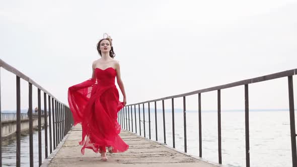 Fashion Young Woman in Long Gown is Fleeing Over Old Ferry Dock Front View