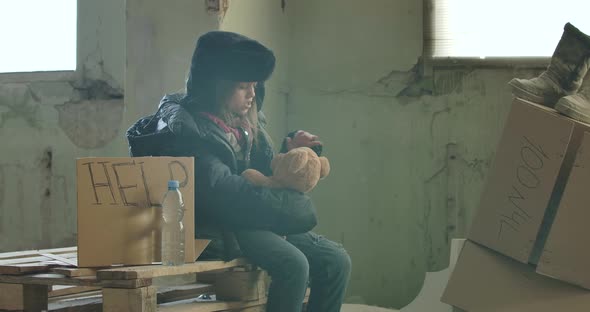 Side View of Ukrainian Refugee in Dirty Clothes Sitting at the Construction Site with Help Cardboard